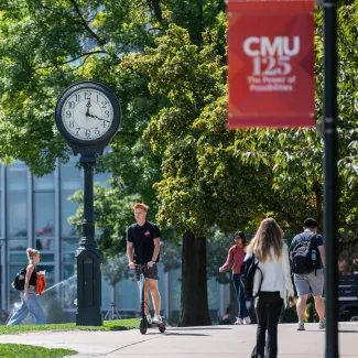Students on campus with a clock and CMU125 banner